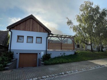 Genussrastplatz der Familie Fröschl in Staatz. Links ist ein zweigeschossiges Presshaus mit weißer Fassade zu sehen, unter dem Presshaus ist eine Garage. Rechts an das Presshaus anschließend ist ein Pergola als Rastplatz.