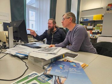 Alexander Ernst und Manuel Denner sitzen vor dem Computer und besprechen Projektunterlagen.