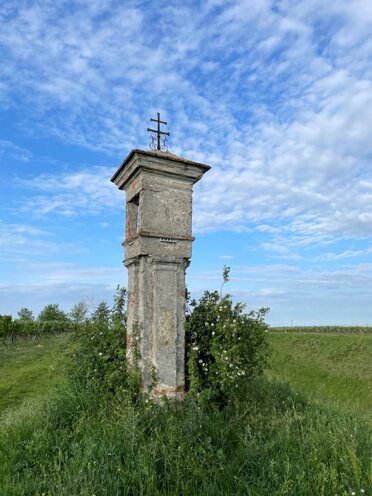 Weißes Marterl auf einem Feld im Grünen.