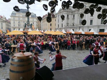 Dreitagesfest am Wiener Hof, von einer Bühne wird auf den Platz fotografiert. Im Hintergrund sind Biergarnituren auf denen viele Menschen feiern mit Weinviertel Sonnenschirmen zu sehen.