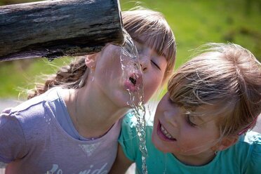 Zwei Mädchen die aus einem Krug Wasser trinken.