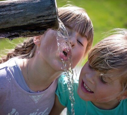 Zwei Mädchen die aus einem Krug Wasser trinken.