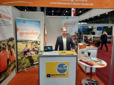 Ein Mitarbeiter von Weinviertel Tourismus am Stand beim Messeauftritt Fiets en Wandelbeurs. Im Vordergrund ist ein weißer Messerstand zu sehen, im Hintergrund zwei Roll ups vom Weinviertel..